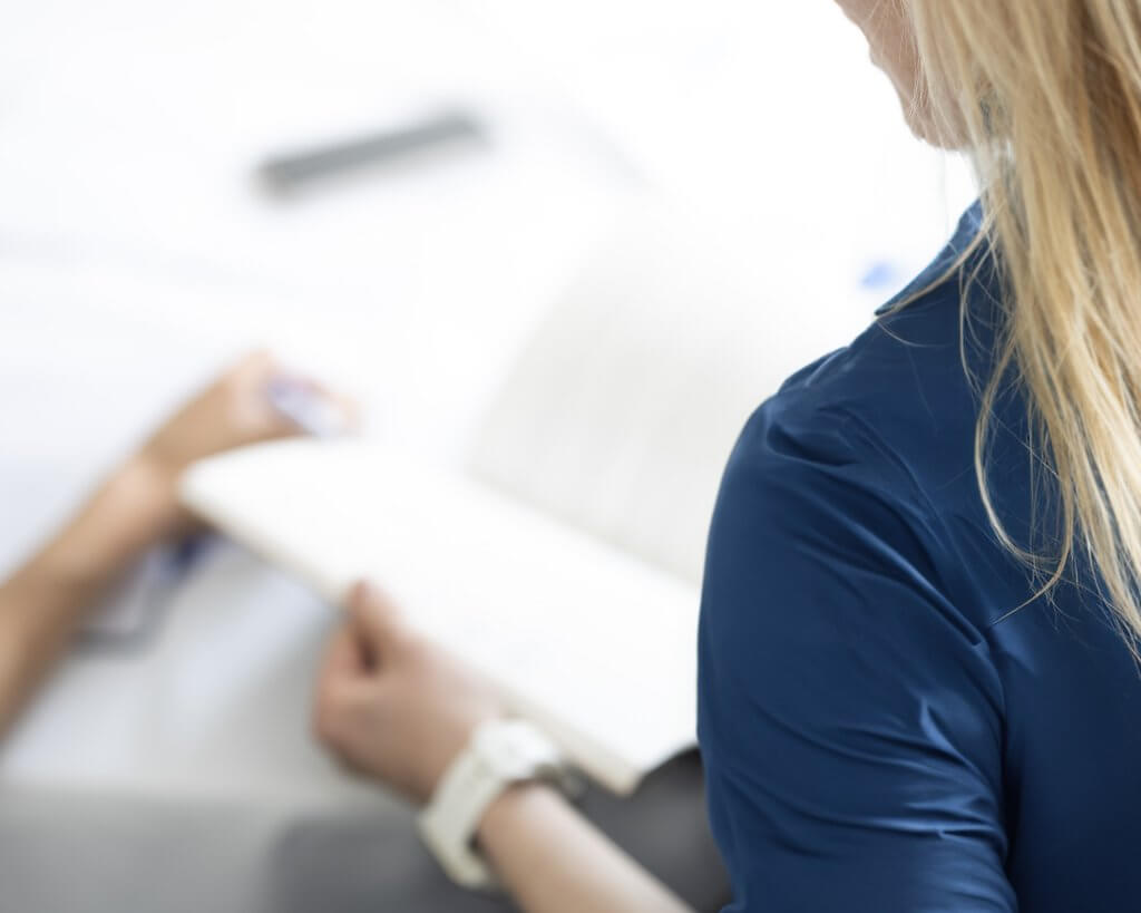 woman in a blue shirt opens a notepad at a conference table