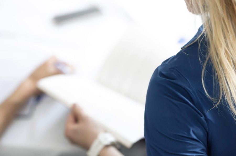 woman in a blue shirt opens a notepad at a conference table