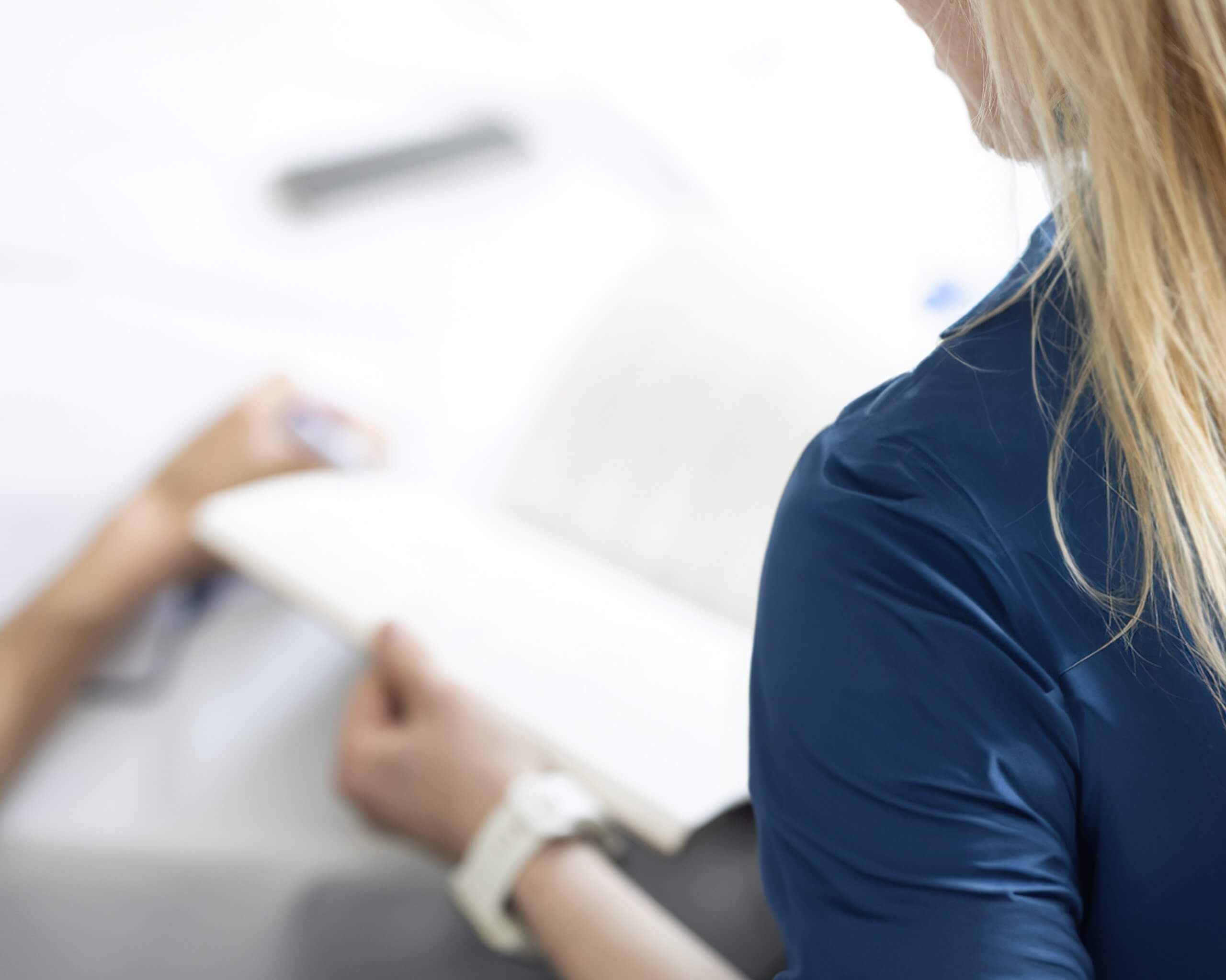 woman in a blue shirt opens a notepad at a conference table